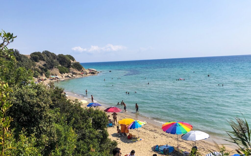 Zonnig zandstrand met kleurrijke parasols en zwemmers nabij Thessaloniki